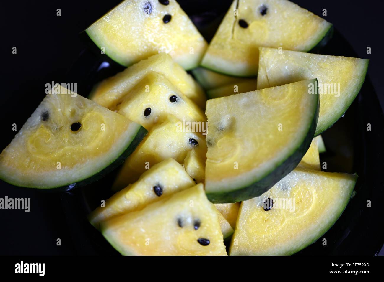 Yellow watermelon cut into triangles on black background Stock Photo