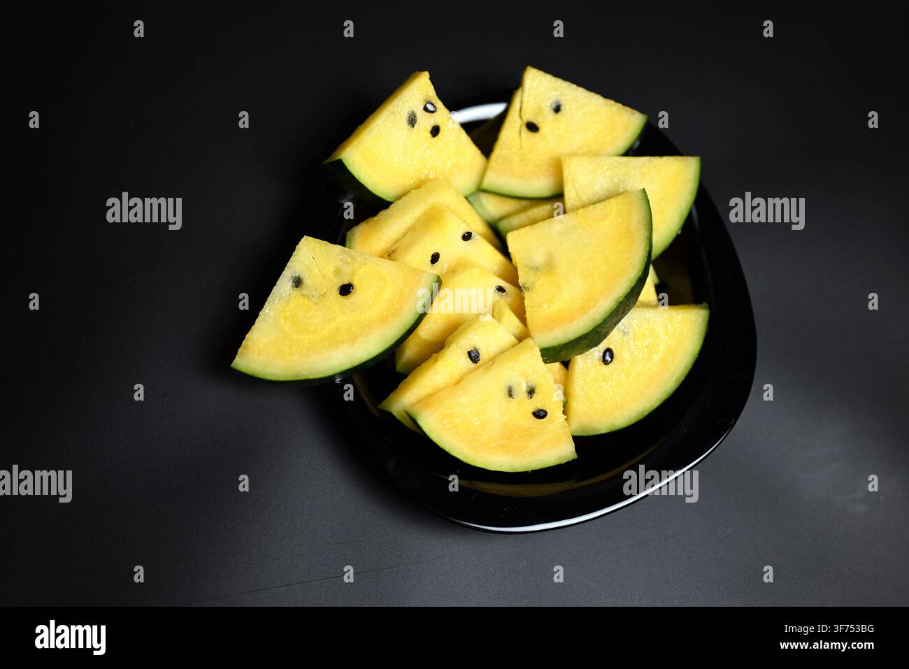 Yellow watermelon cut into triangles on black background Stock Photo