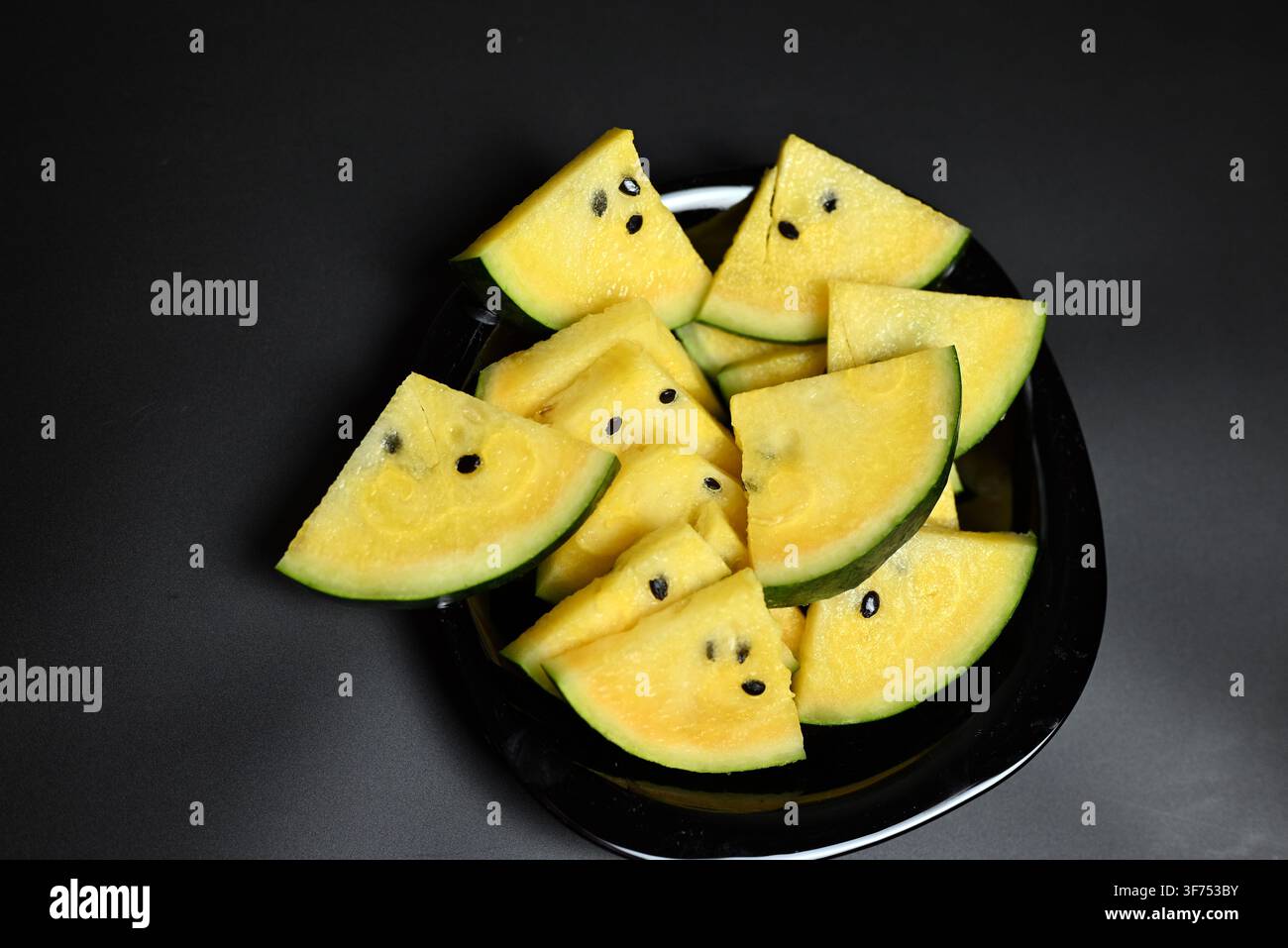 Yellow watermelon cut into triangles on black background Stock Photo