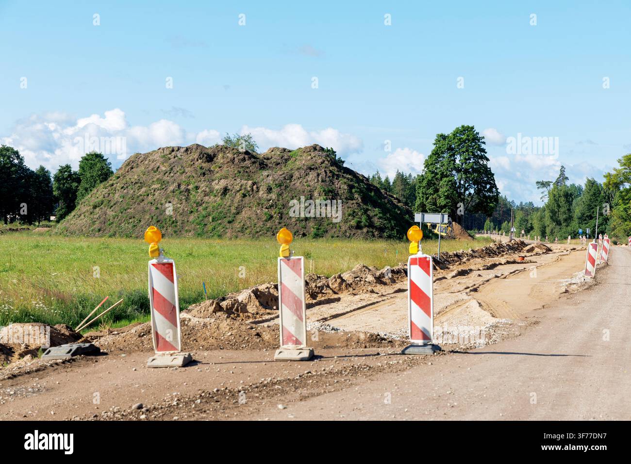 Close up view of red and white traffic warning posts on a gravel road next to large dirt mounds. Stock Photo