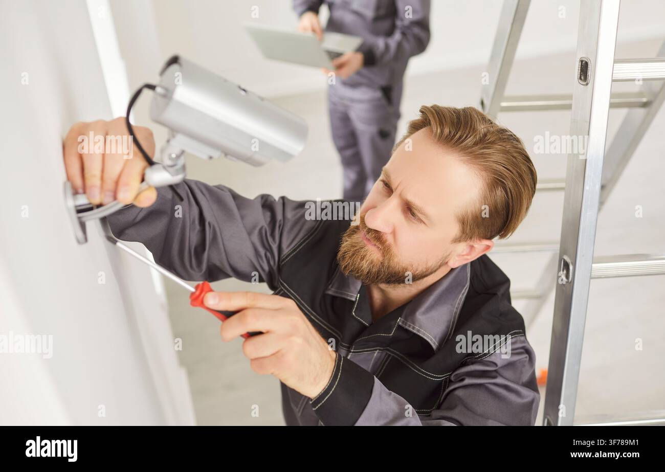 Portrait of young technician man installing surveillance CCTV camera on wall indoors Stock Photo