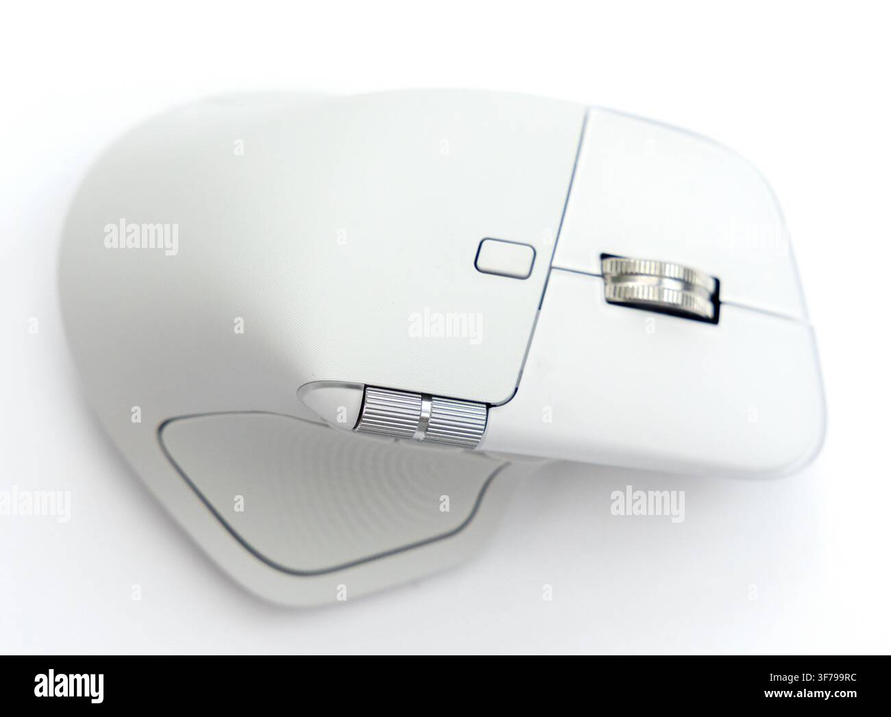 A modern wireless computer mouse rests on a clean white surface Stock Photo