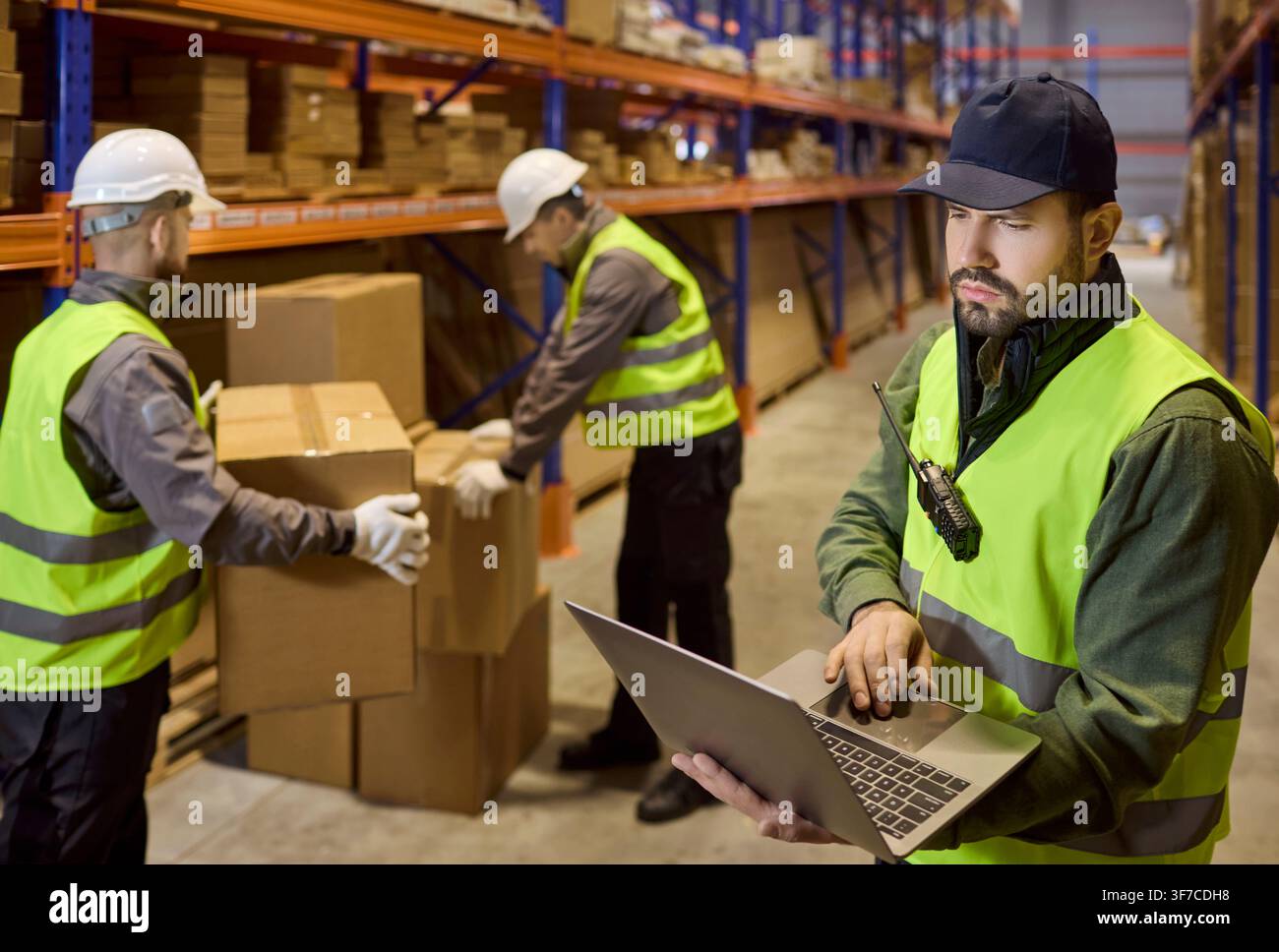 Warehouse manager using laptop while team handles boxes during stock inventory Stock Photo