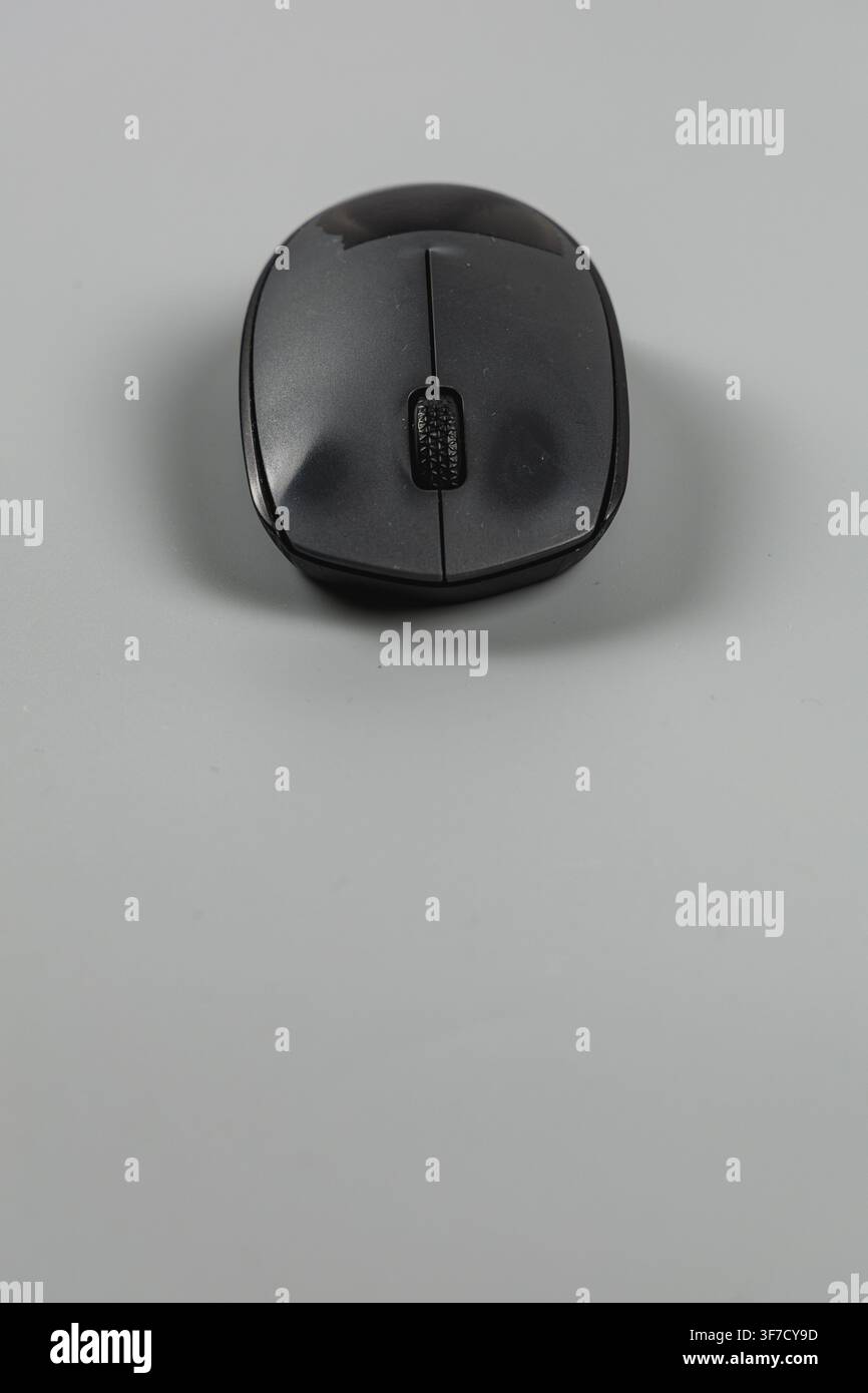 A wireless computer mouse sits on a plain surface in an office setting. It is ready for work. Stock Photo