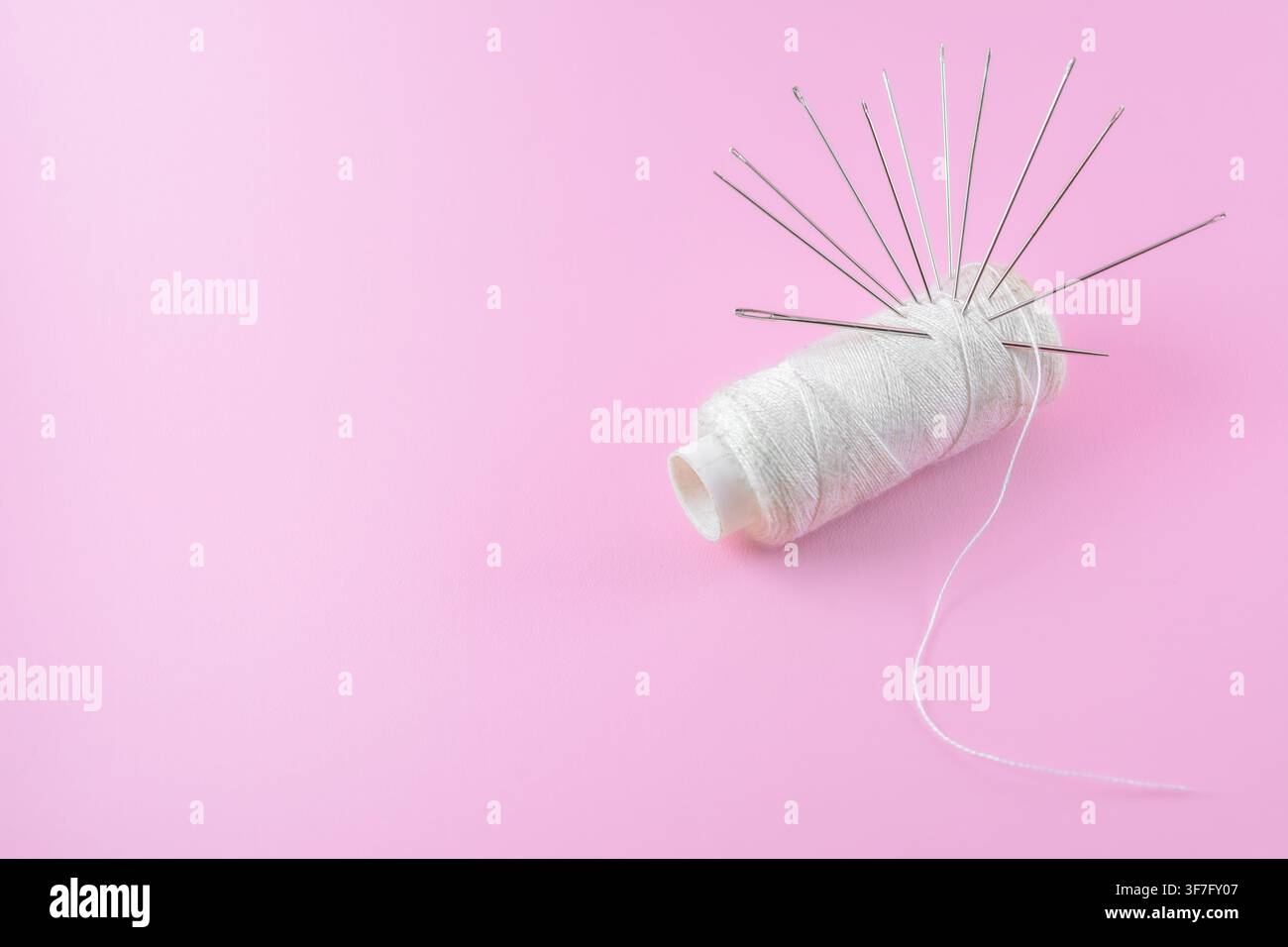 Traditional Sewing tools, needles and white thread isolated pink background Stock Photo
