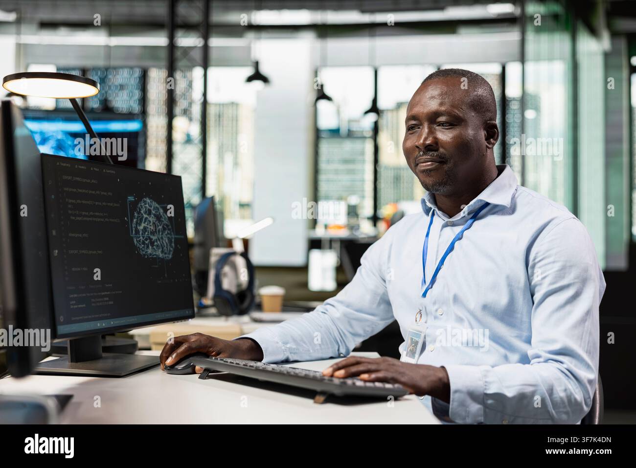Smiling programmer in AI tech company workplace using PC to conduct code reviews. Happy IT professional using computer program at office desk to design and implement machine learning algorithms Stock Photo