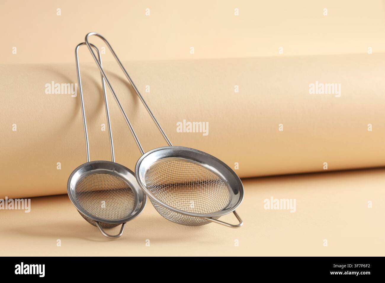 Two stainless steel mesh strainers with long handles for kitchen and cooking use on a beige background Stock Photo