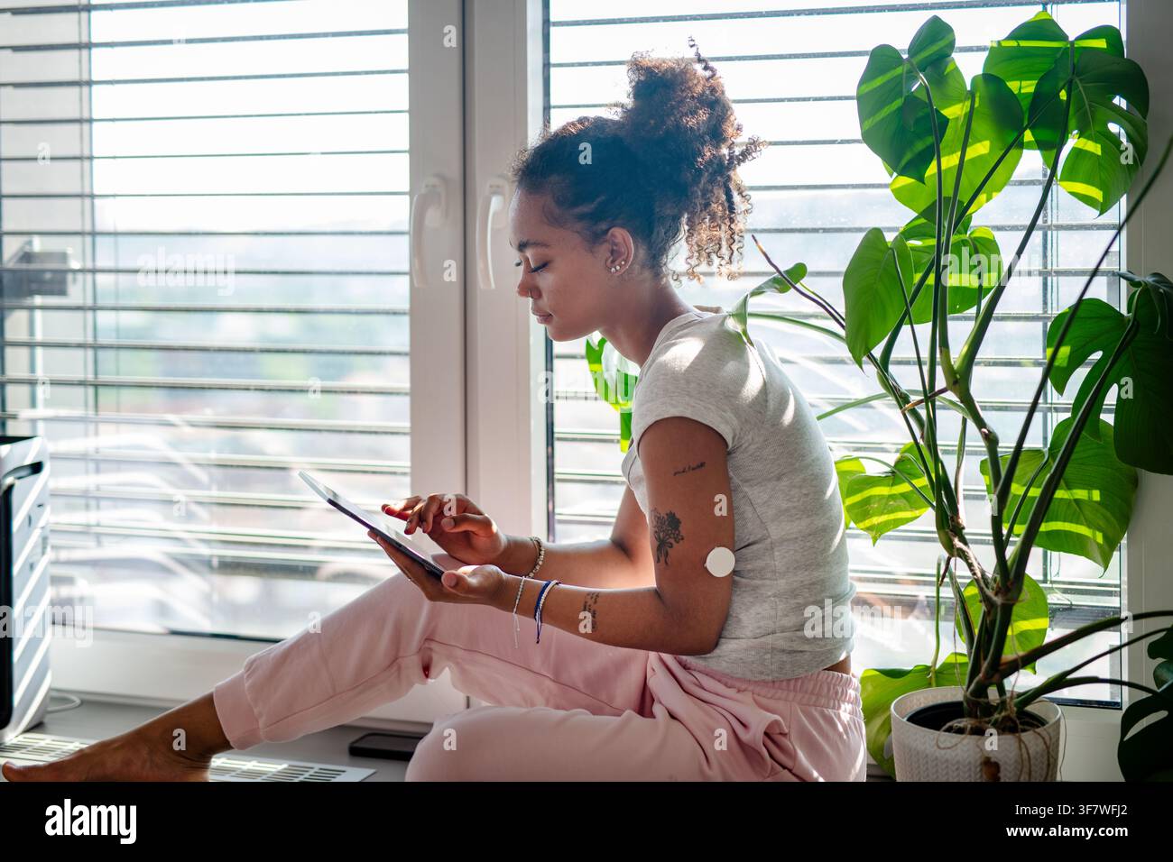 Female diabetes patient with CGM sensor using tablet in bright apartment Stock Photo
