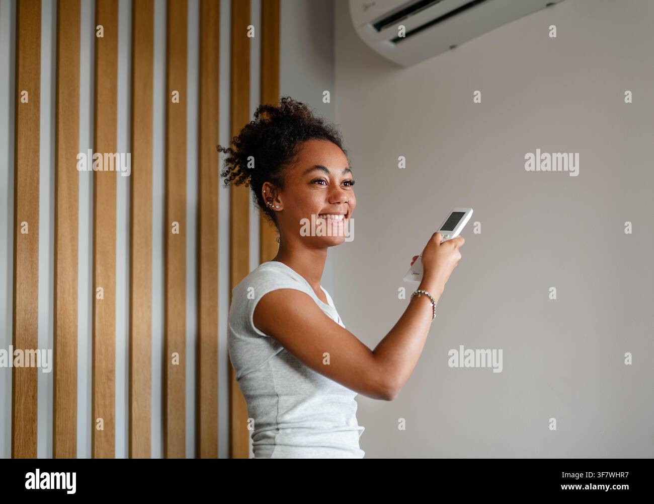 Young woman setting home temperature using air conditioner remote. Stock Photo