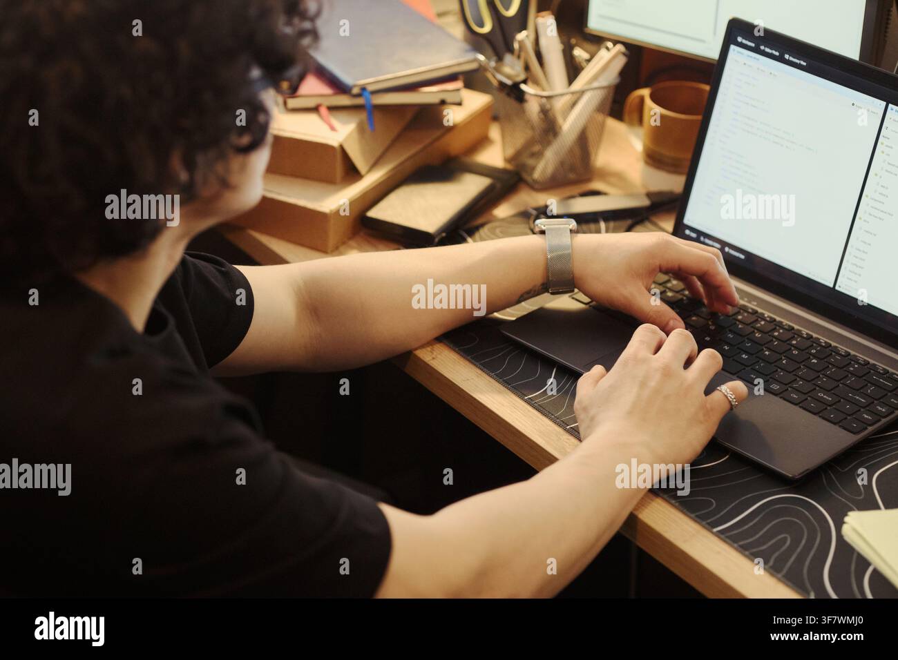 young man typing on laptop keyboard at wooden desk, writing software code. Over shoulder view representing remote work, programming education, and software development services Stock Photo