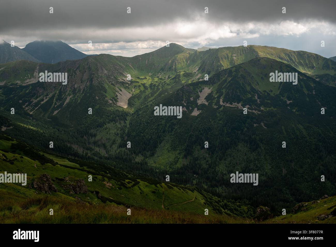 Sun breaking through storm clouds over green mountains Stock Photo
