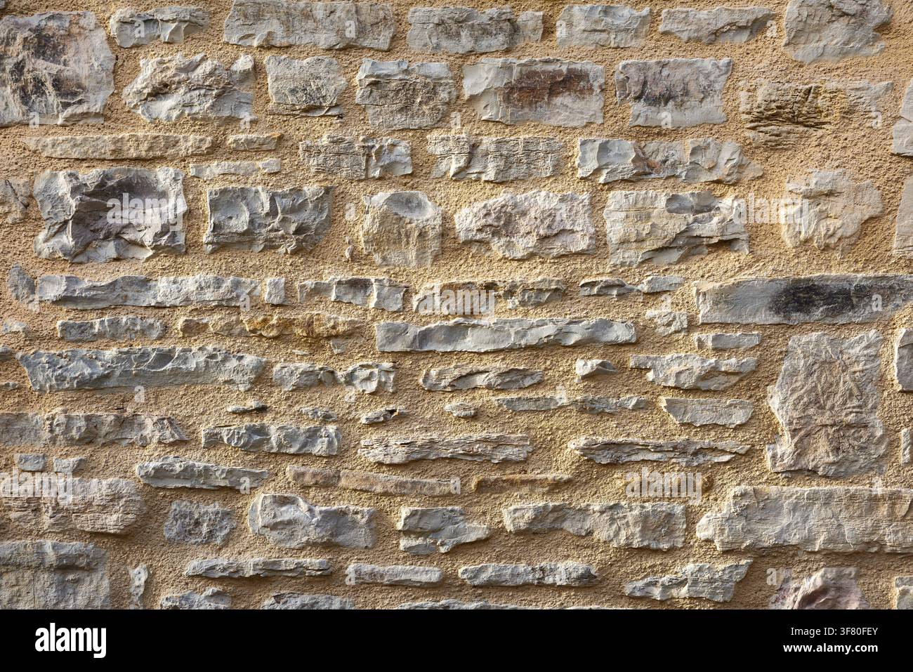 Wall of horizontally aligned gray stones held together with brown cement. Front view. Stock Photo