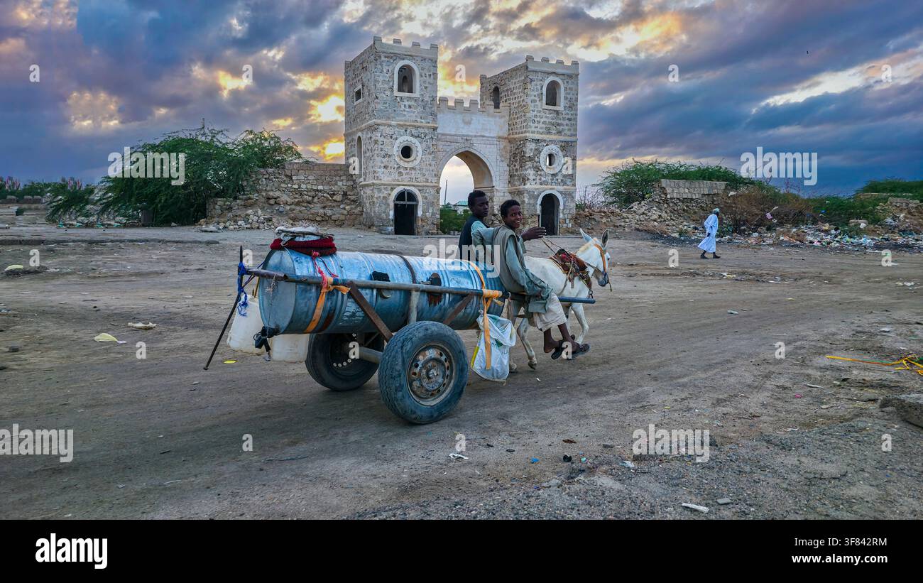 Boys riding a horse cart near a historic city gate at Suakin Island during sunset in Sudan Stock Photo