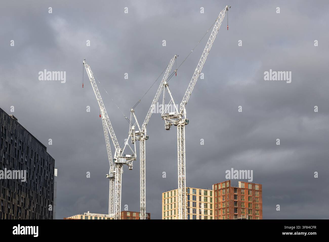 Construction cranes against cloudy sky in urban development Stock Photo