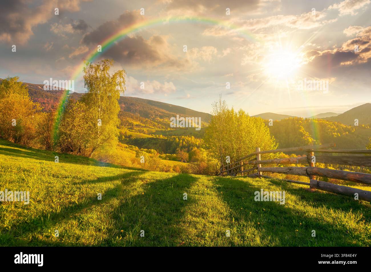 sunset over mountainous rural landscape in spring. lovely view of valley fields. alpine meadow in evening light. carpathian mountains countryside with Stock Photo