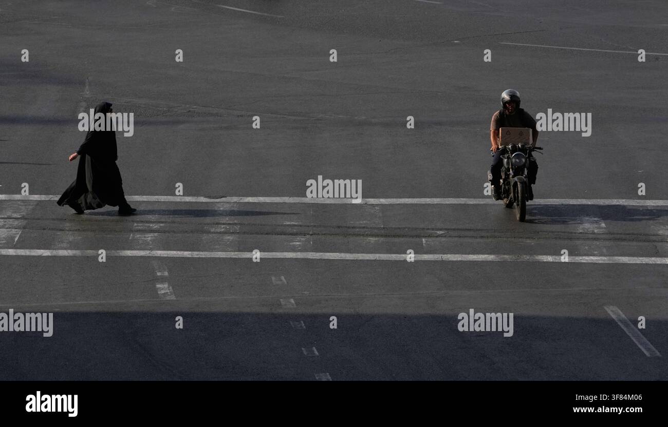 A woman walks as a motorbike drives at a square in Tehran, Iran, Monday ...