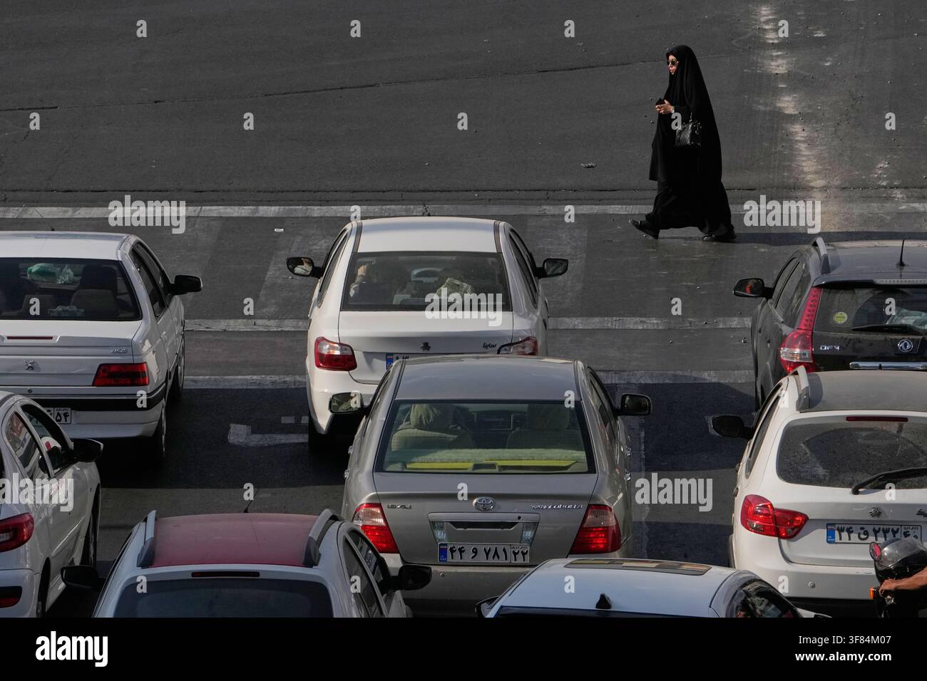 A woman crosses a square as vehicles wait for the green light in Tehran ...