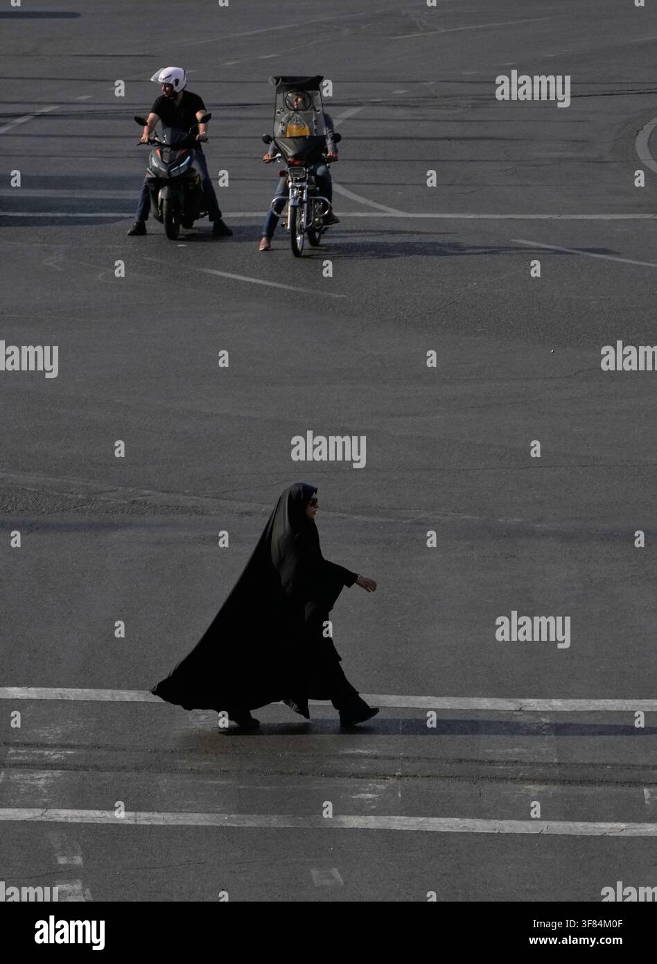 A woman crosses a square as motorbikes wait for the green light in ...