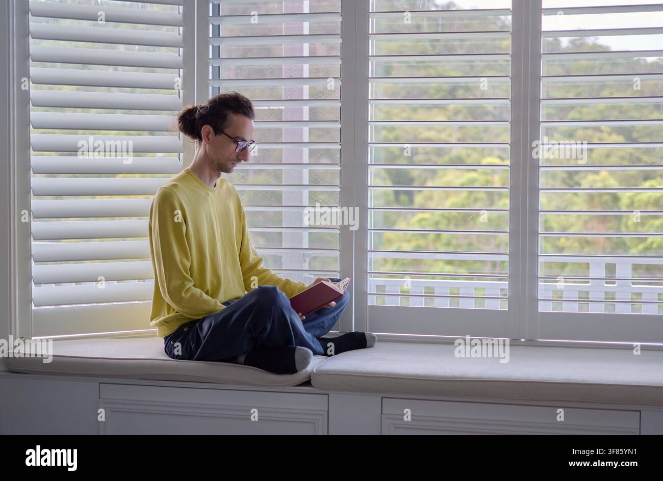 Man Reading Book While Sitting on Window Seat at Home Stock Photo