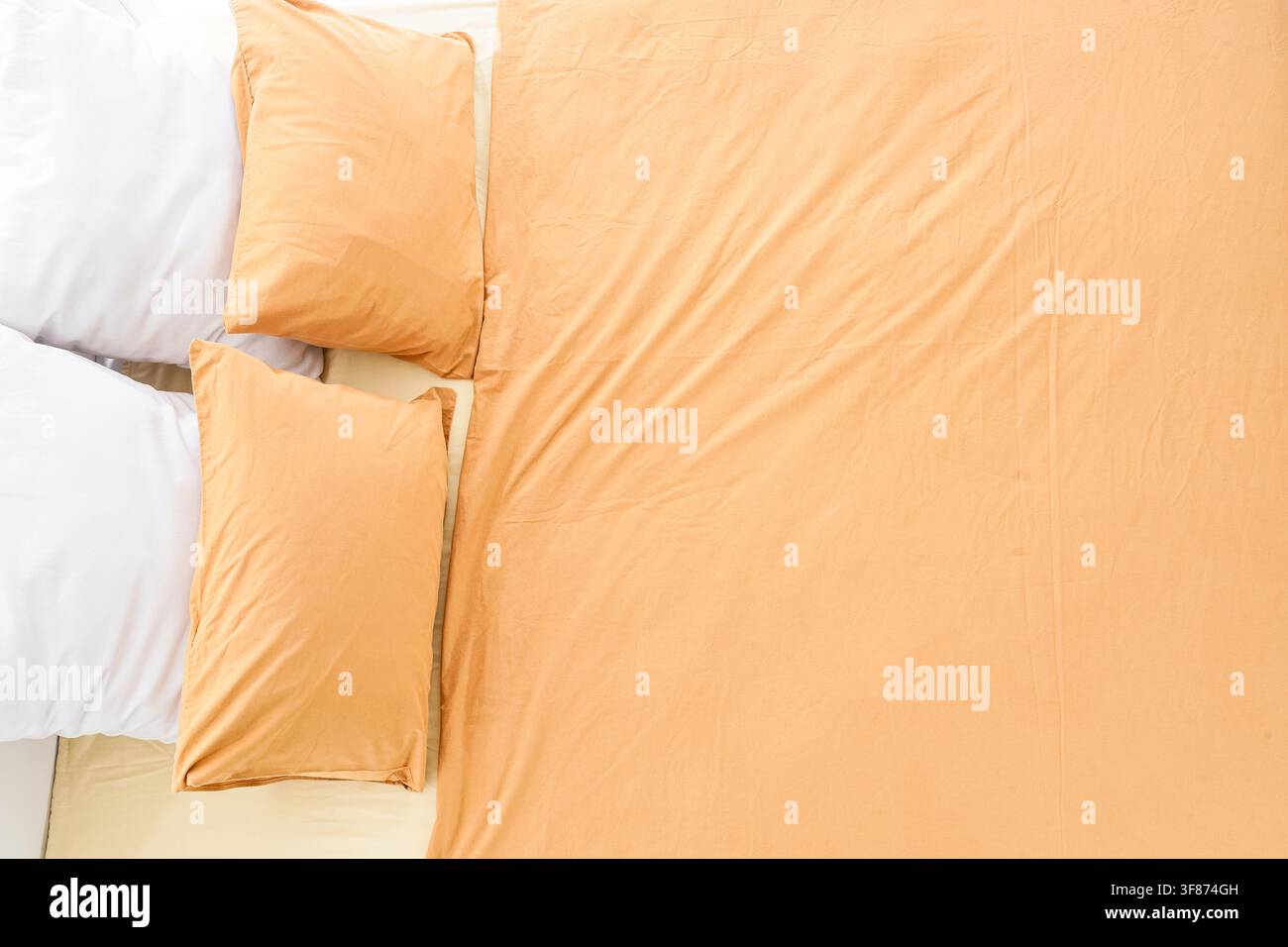 Top down view of a bed with two white pillows and two orange pillows on a light orange sheet, comfortable bedding Stock Photo