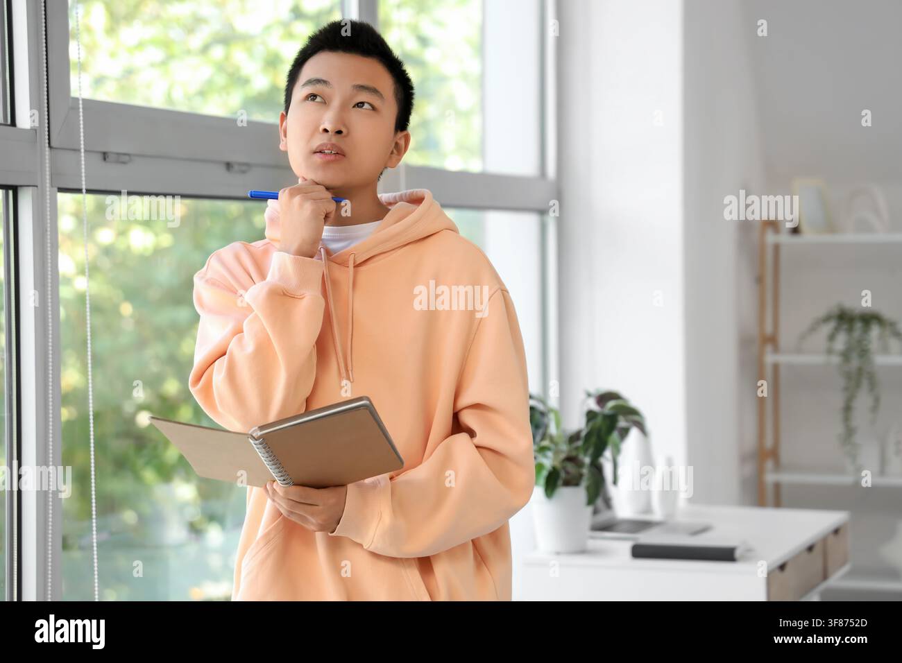 Thoughtful young Asian man with notebook at home Stock Photo
