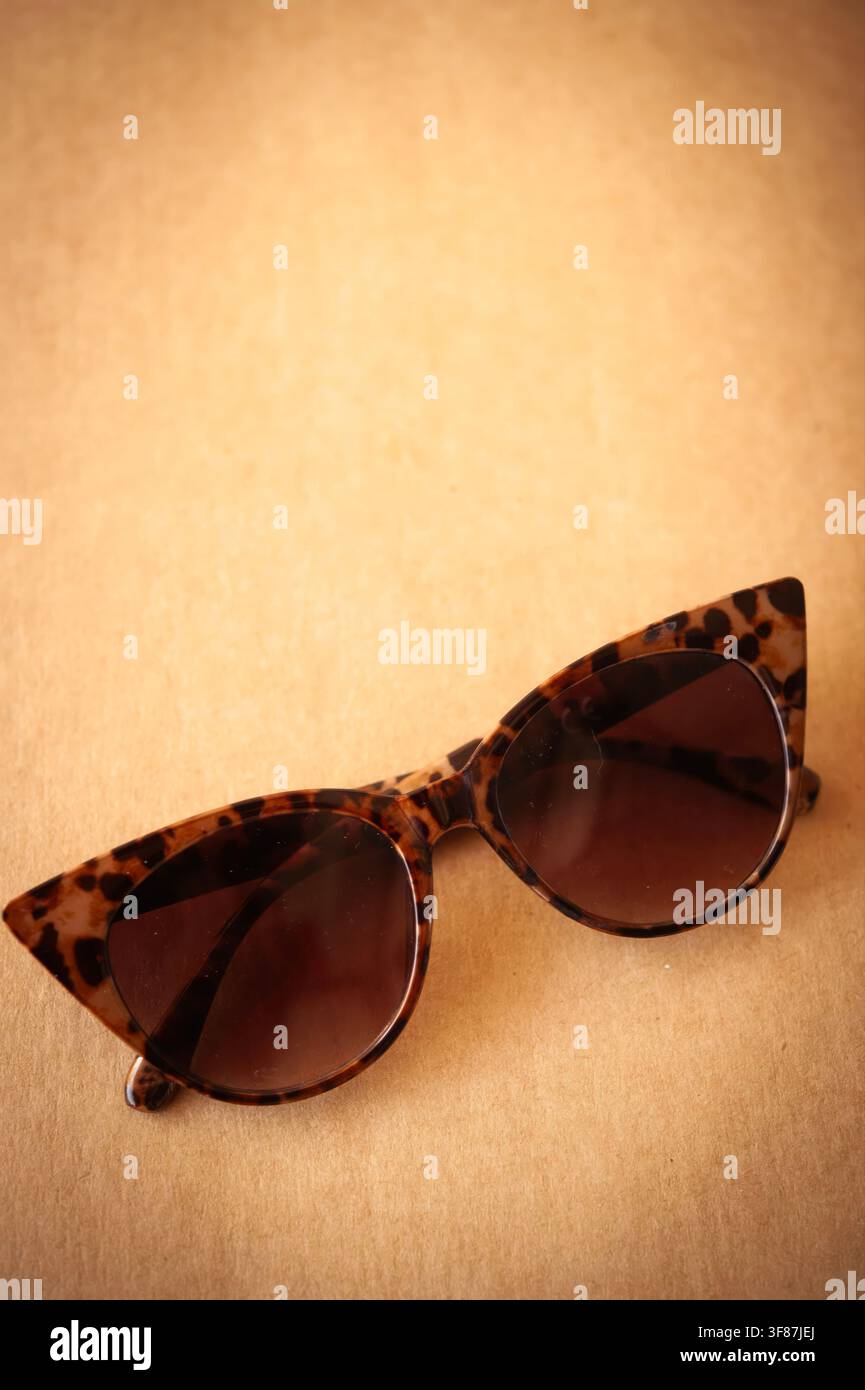 Tortoiseshell cat-eye sunglasses resting on a warm brown surface with soft background blur and generous copy space Stock Photo