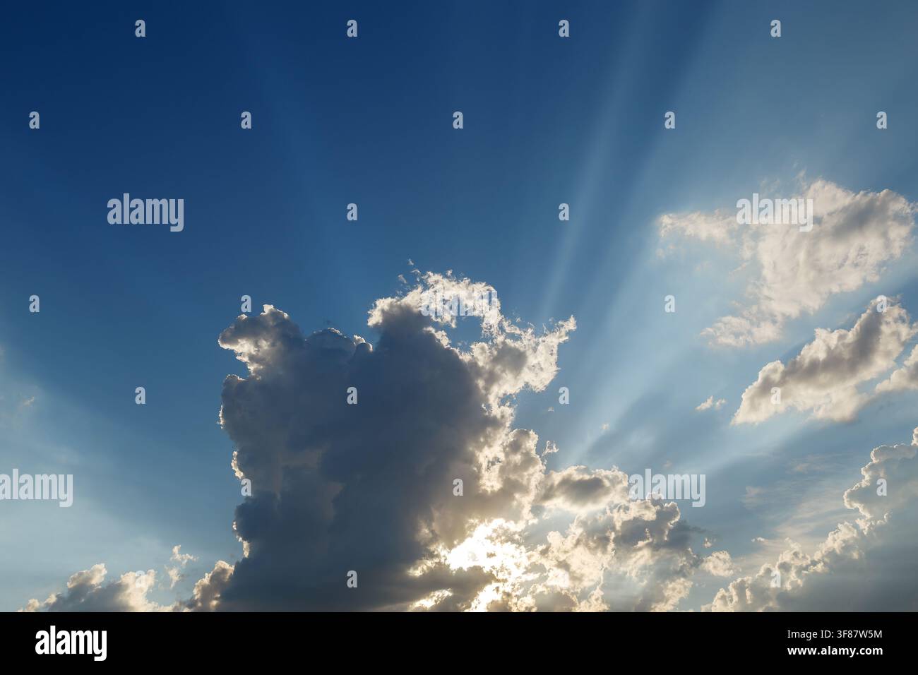Dramatic blue sky with sun rays shining through fluffy white clouds Stock Photo