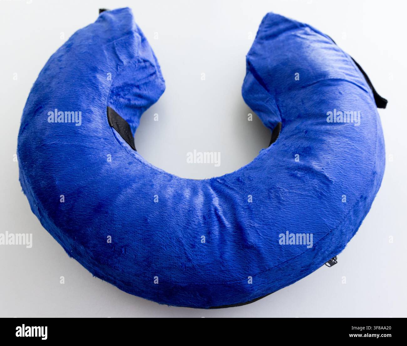 A fluffy blue Ushaped neck pillow rests on a white background Stock Photo