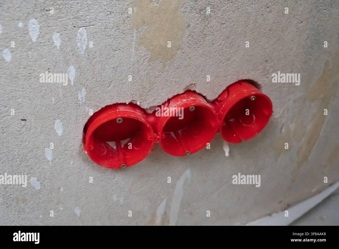 Red electrical junction boxes recessed into a gray concrete wall during renovation, ready for wiring and outlets as part of residential construction a Stock Photo
