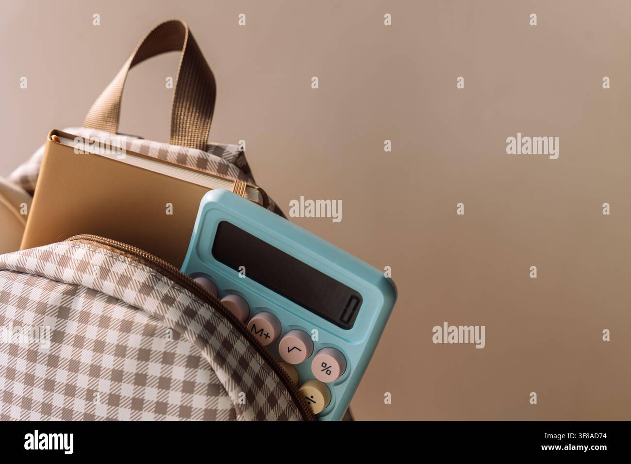 Checkered school backpack with notebook and blue calculator in warm light Stock Photo