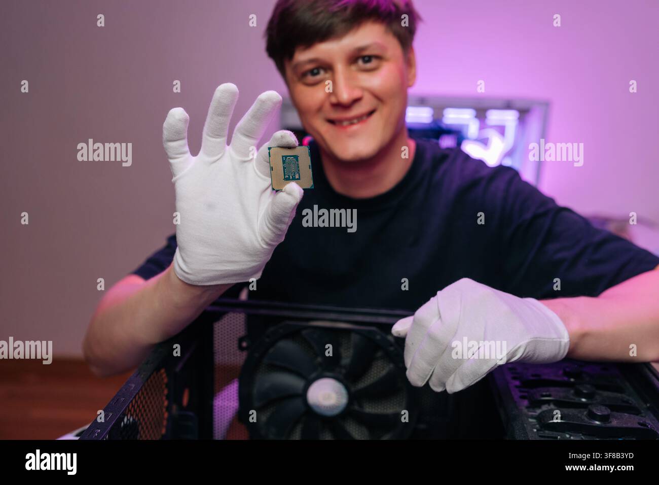 Smiling man wearing white protective gloves holding up central processing unit, demonstrating computer hardware for technology and maintenance Stock Photo