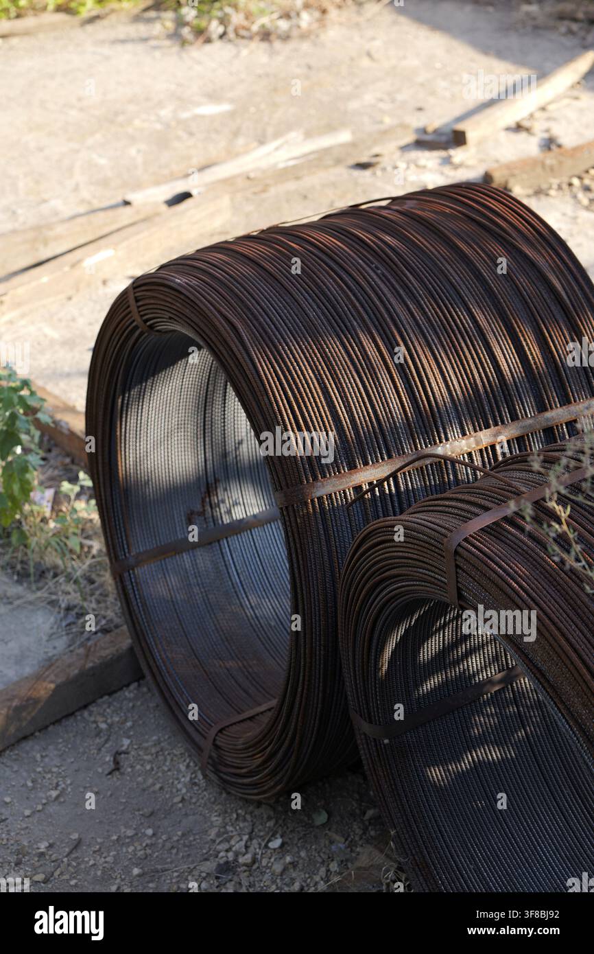 Two large rolls of rusty steel rebar, bound together with metal strapping, stand ready for use as essential building materials in an industrial settin Stock Photo