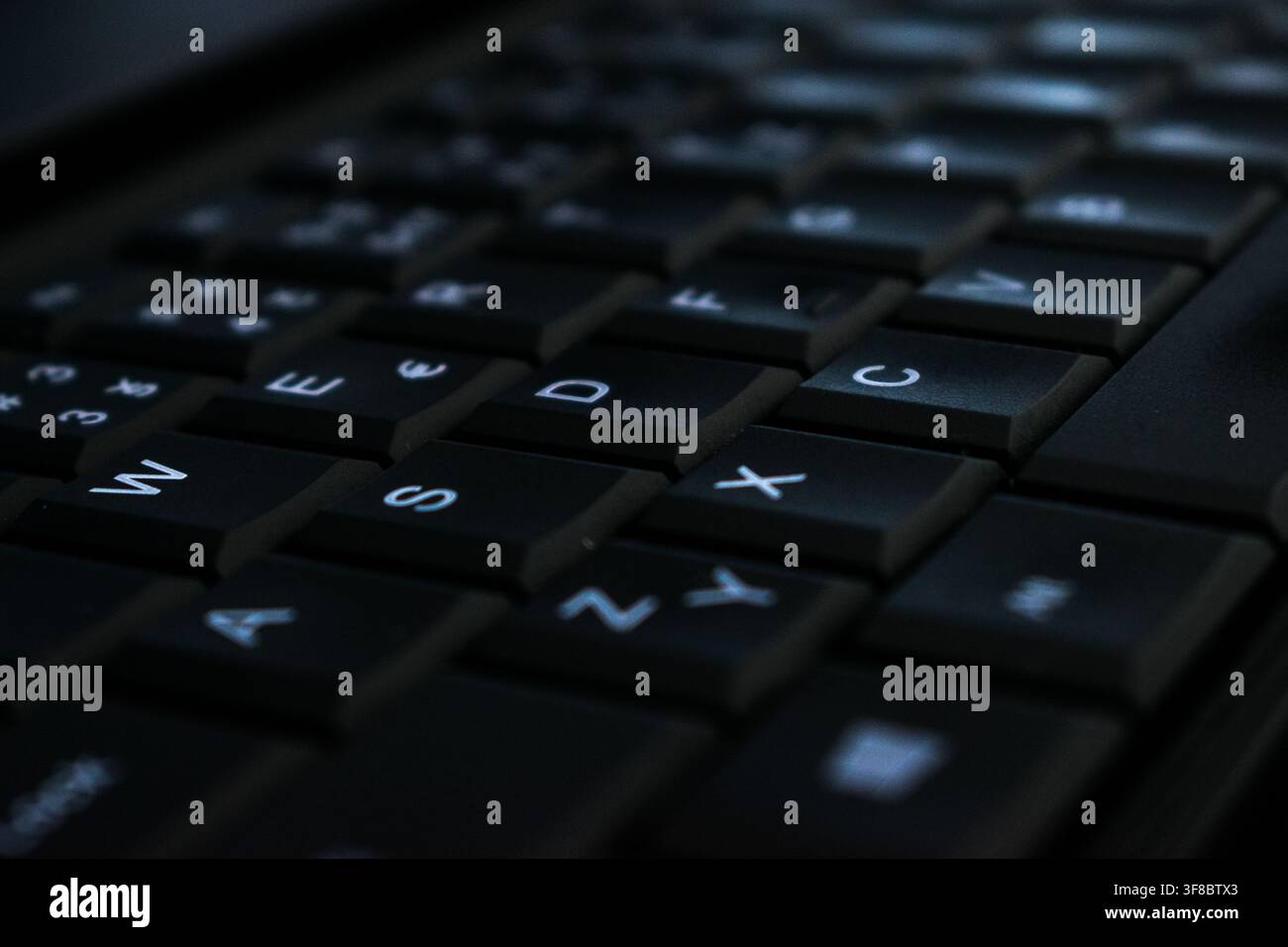 Extreme close-up of backlit black laptop keyboard keys at an angle Stock Photo