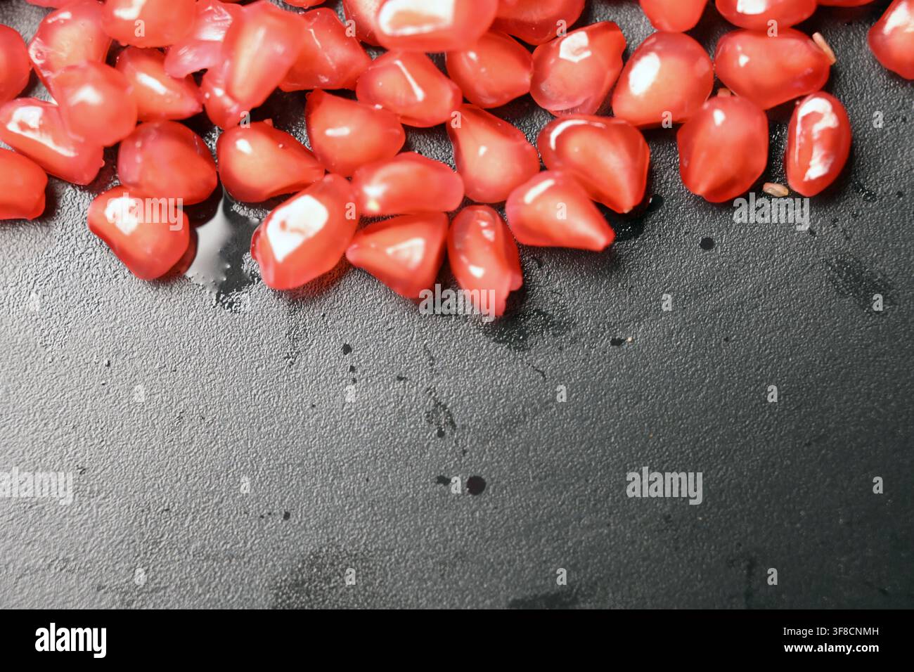 Glossy Ruby Pomegranate Seeds on Black Stone Backgrounds Stock Photo