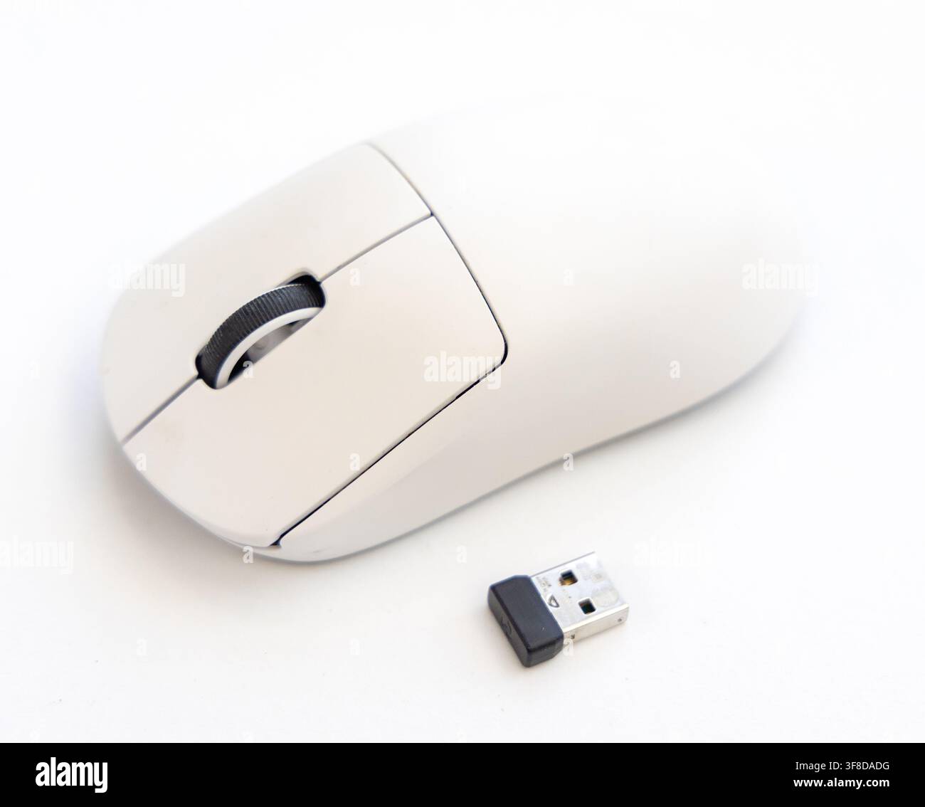 A white wireless computer mouse sits next to its USB receiver Stock Photo