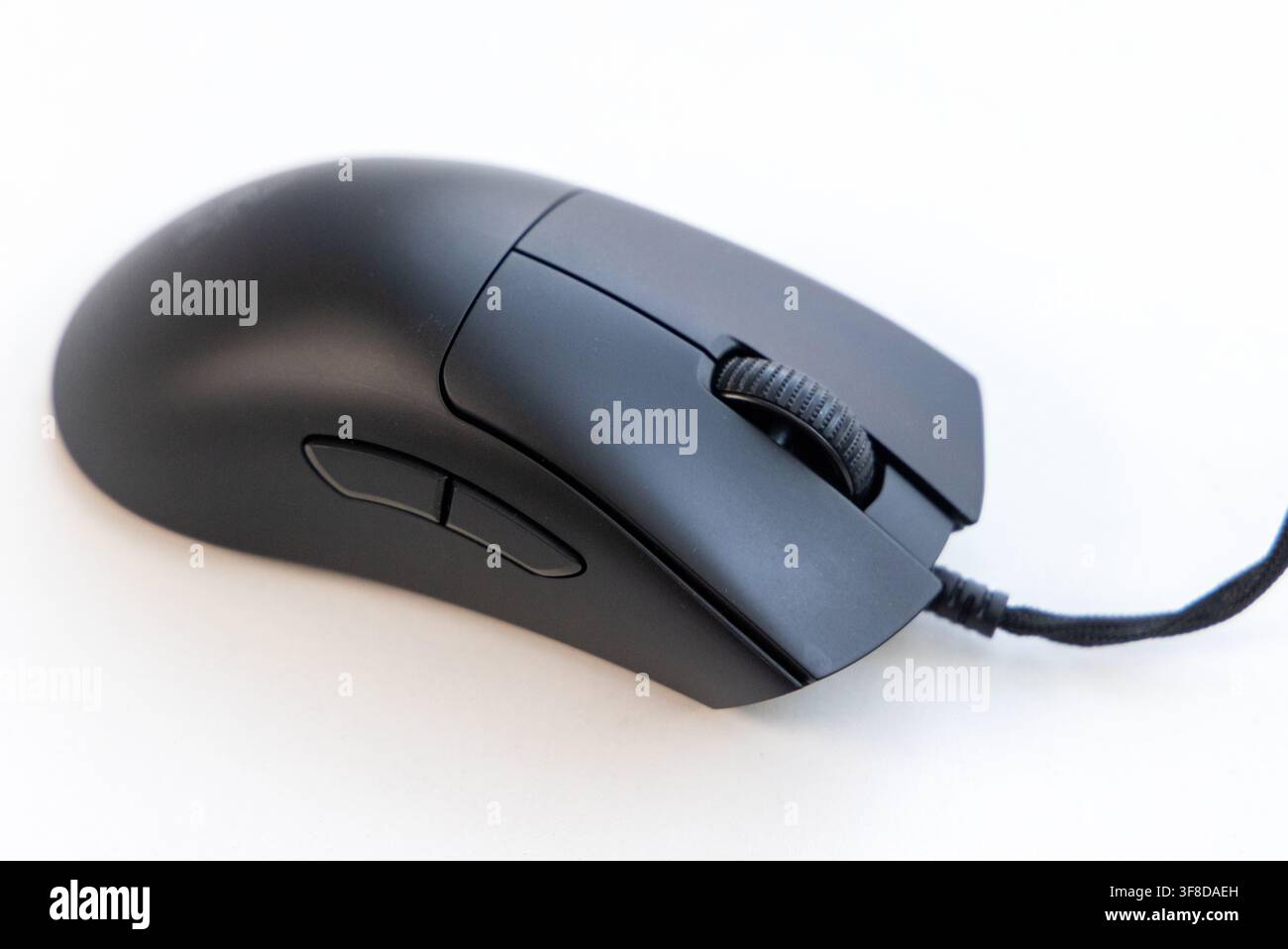 A modern black computer mouse sits on a white surface Stock Photo