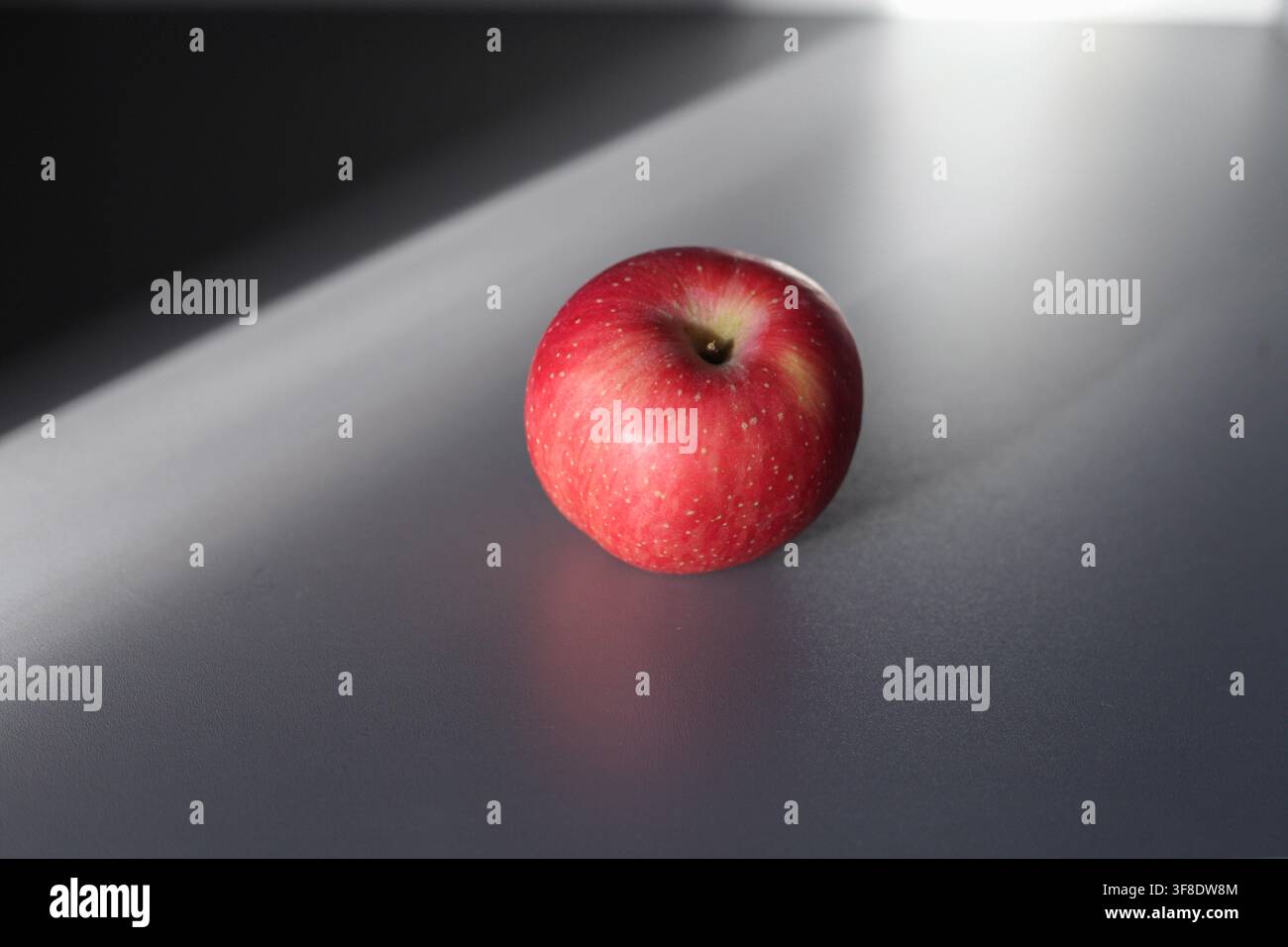 Single red apple on dark surface with dramatic window light Stock Photo