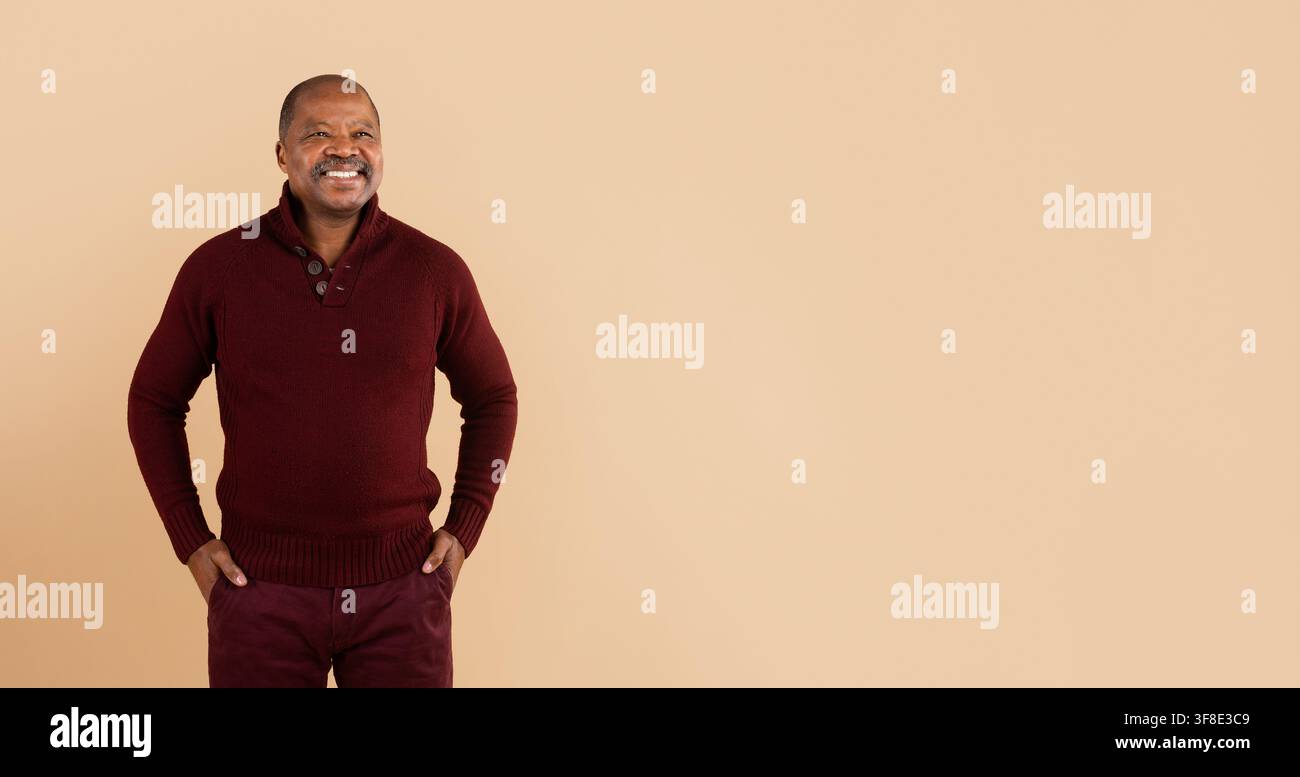 Cheerful black man in burgundy sweater looking away with hands in pockets Stock Photo