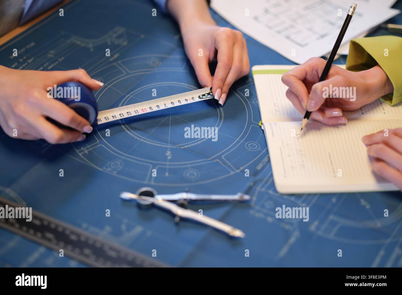 Engineer measures detail on blueprint as colleague marks notes Stock Photo