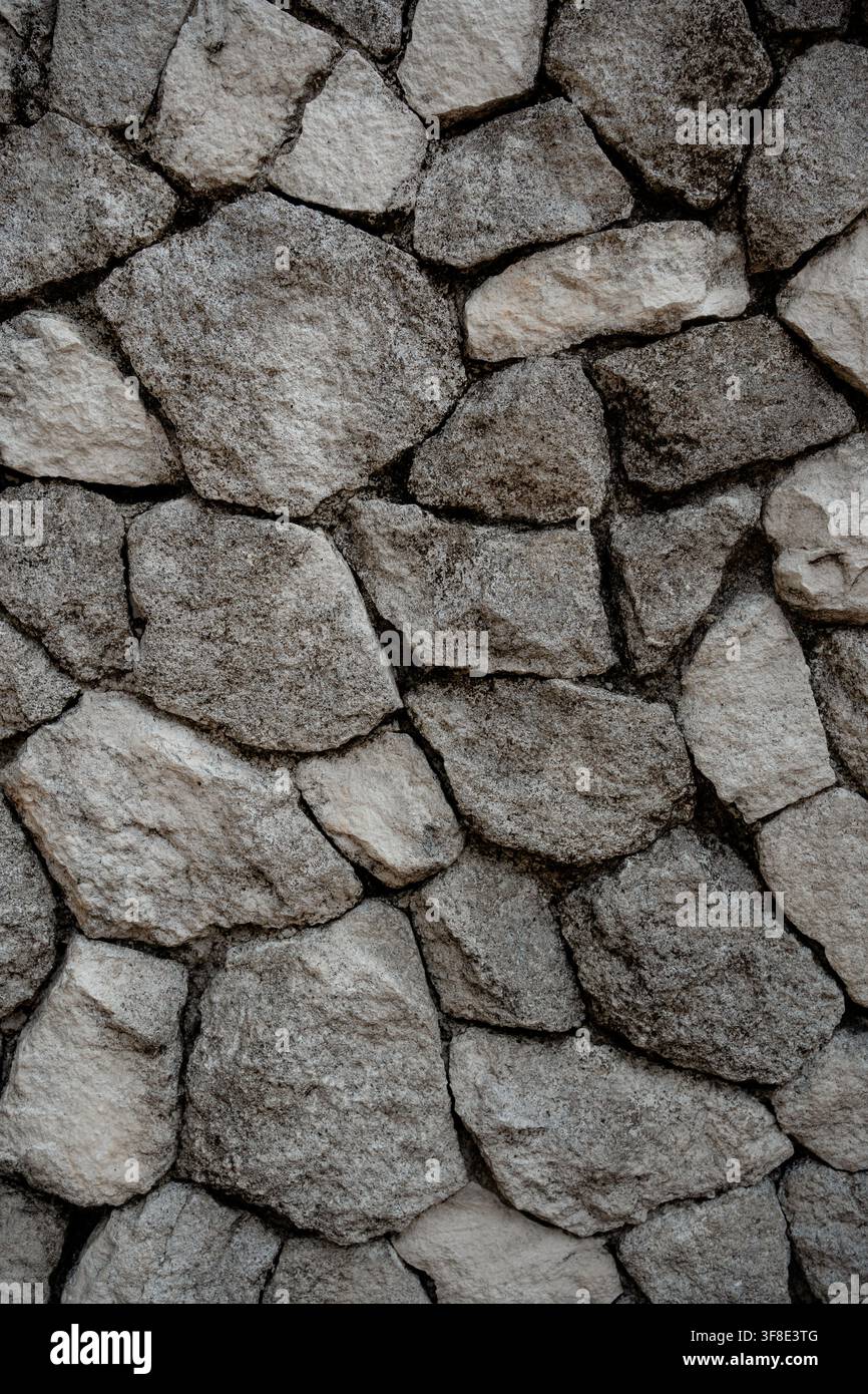 Stone wall texture featuring irregular grey rocks in vertical composition. Stock Photo