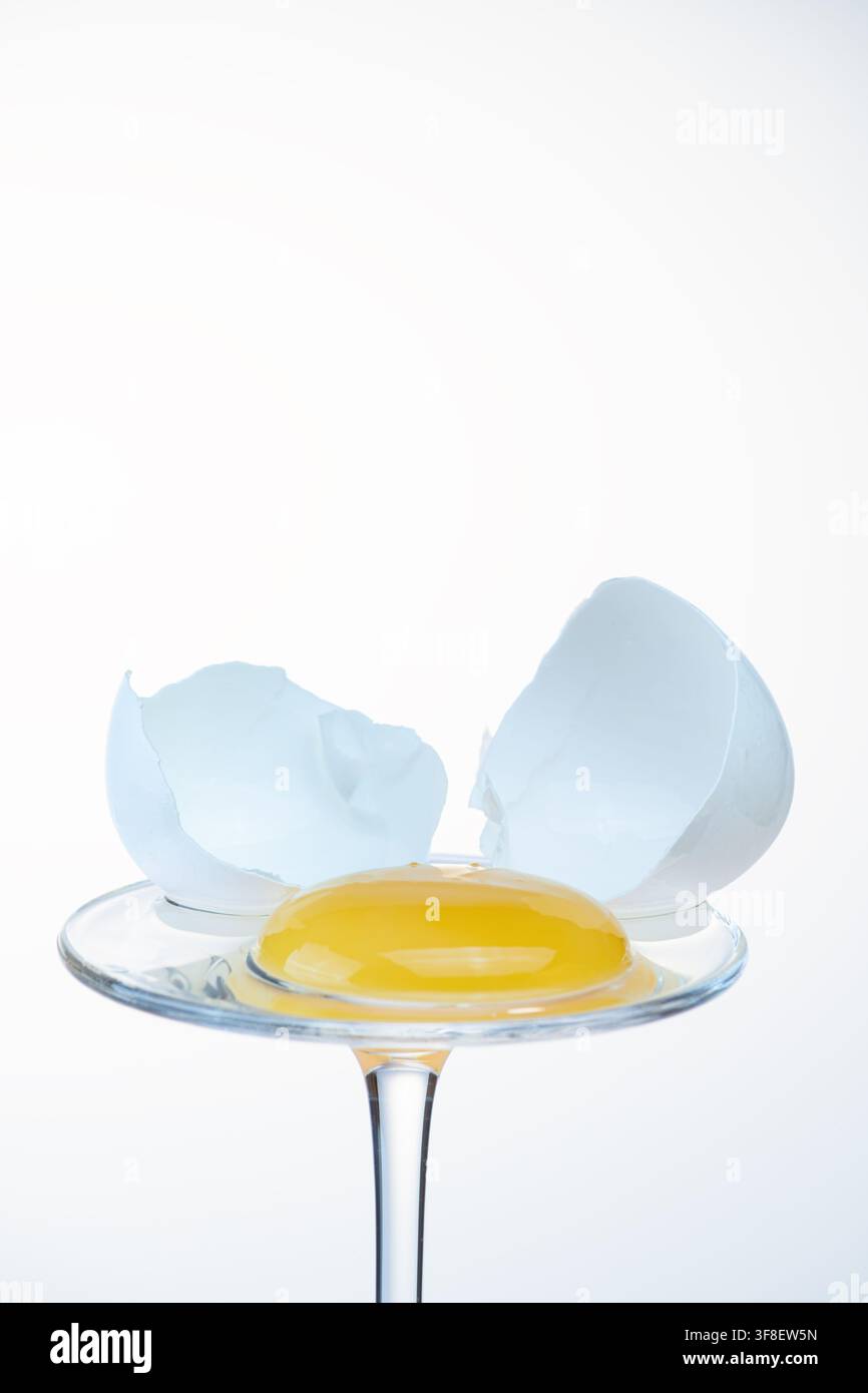 Egg yolk on a glass coupe with cracked shell opened wide on both sides, bright background Stock Photo