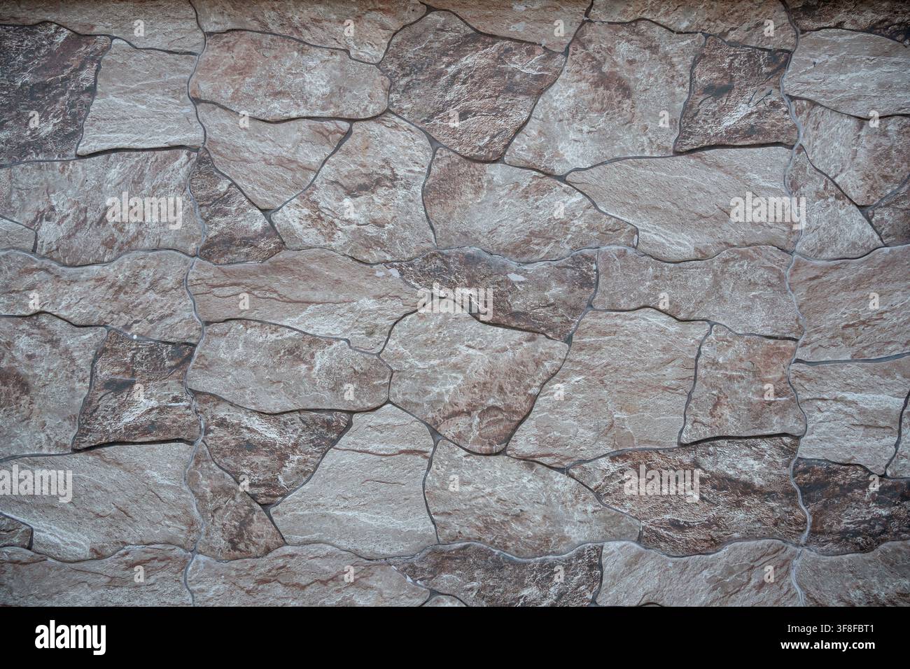 Stone wall texture with irregular brown and gray slate tiles pattern. Stock Photo