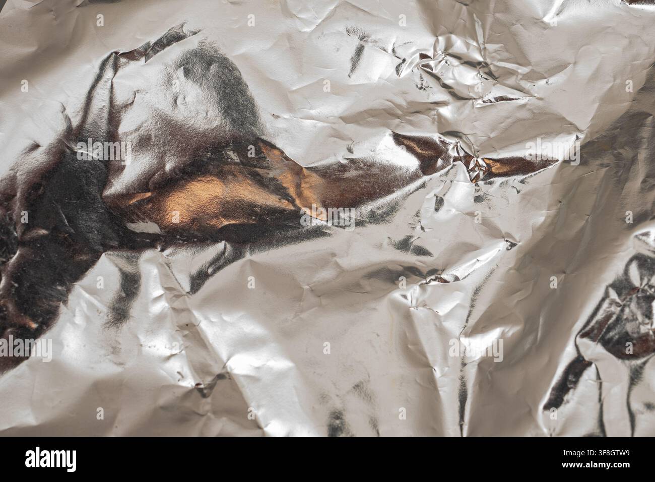 A piece of metal foil is crumpled on a flat surface. The surface reflects light, creating unique textures and patterns. This shows the details of the Stock Photo