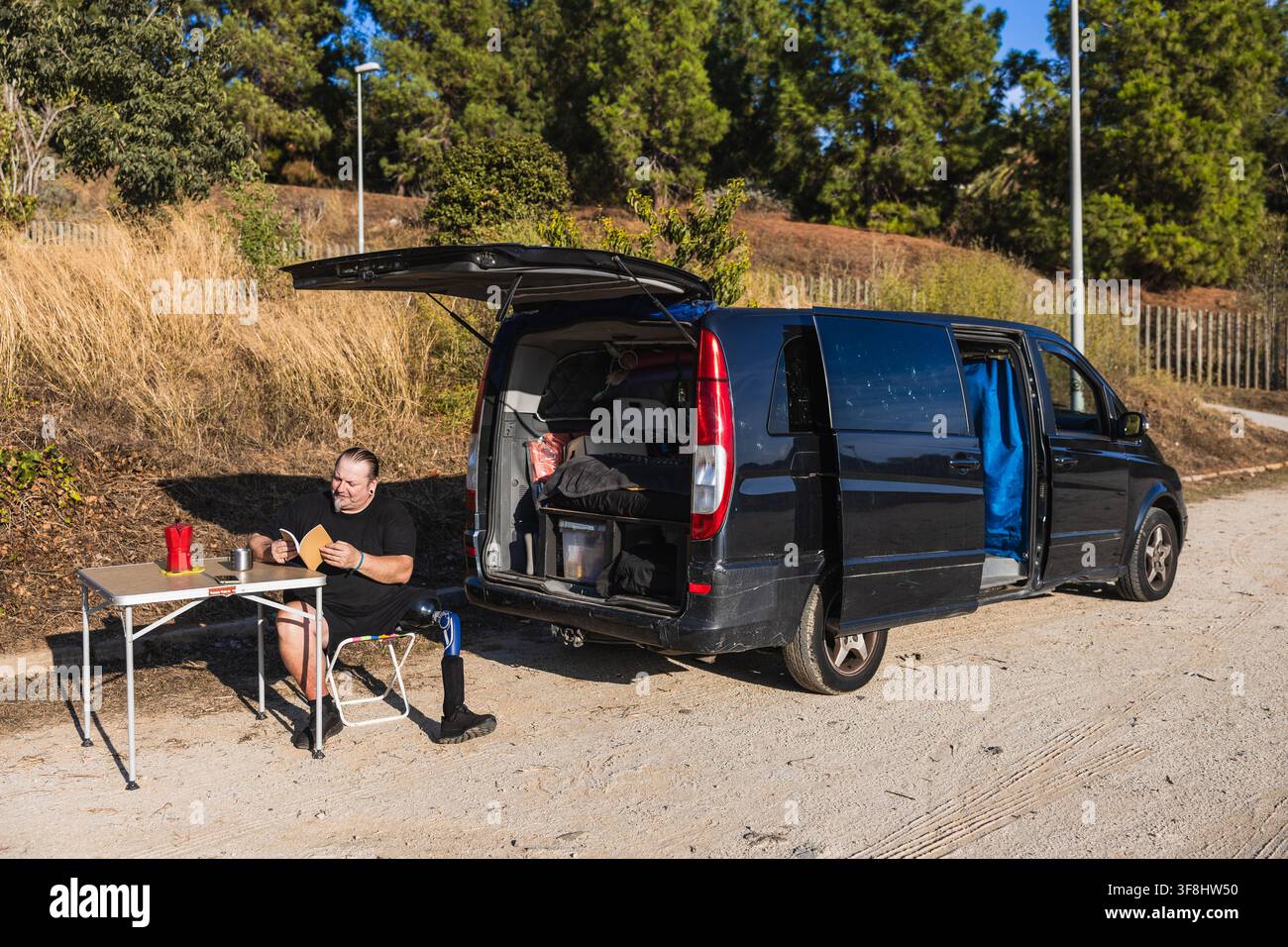 Amputee man enjoying van life outdoors reading book Stock Photo