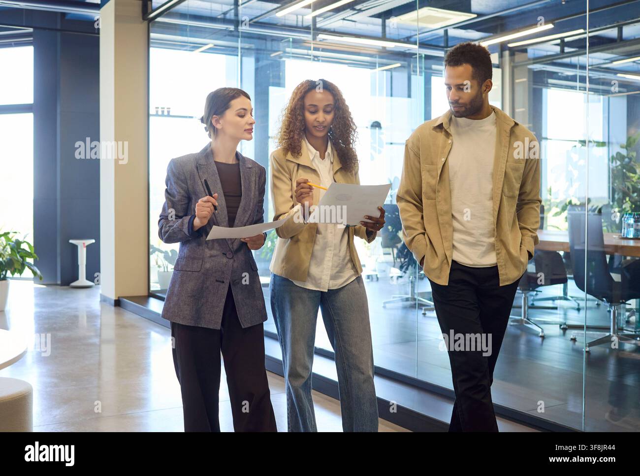 Three colleagues walking in modern office, discussing documents and planning Stock Photo