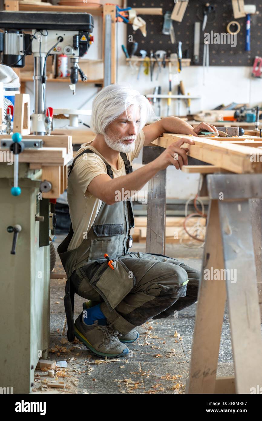 Passionate craftsman attentively checking surface of antique wooden door at worktable in workshop Stock Photo