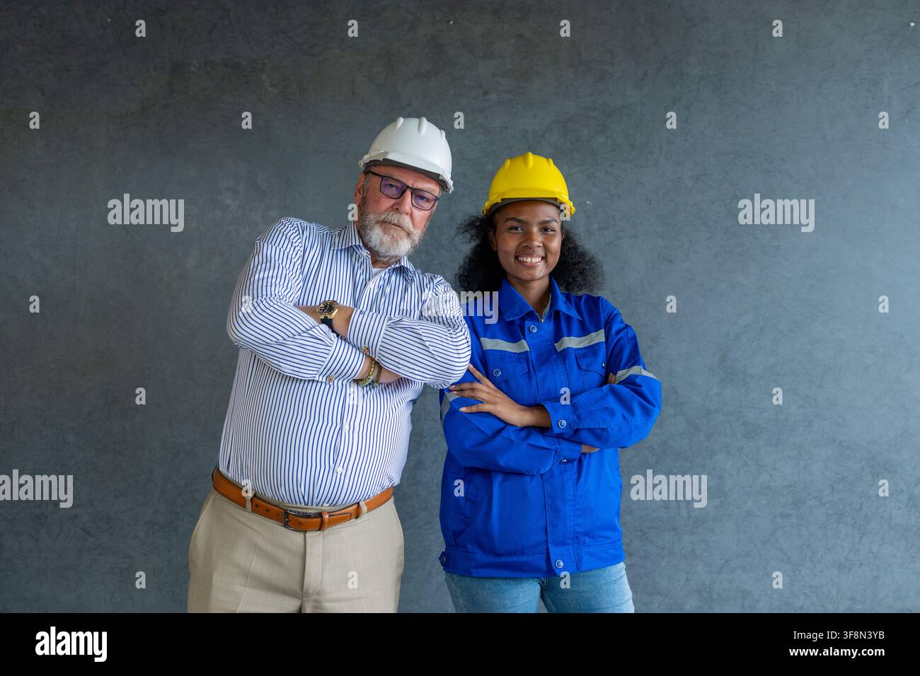 Engineer senior and woman engineer wearing safety helmets discussing blueprints in office collaborating on construction. Stock Photo