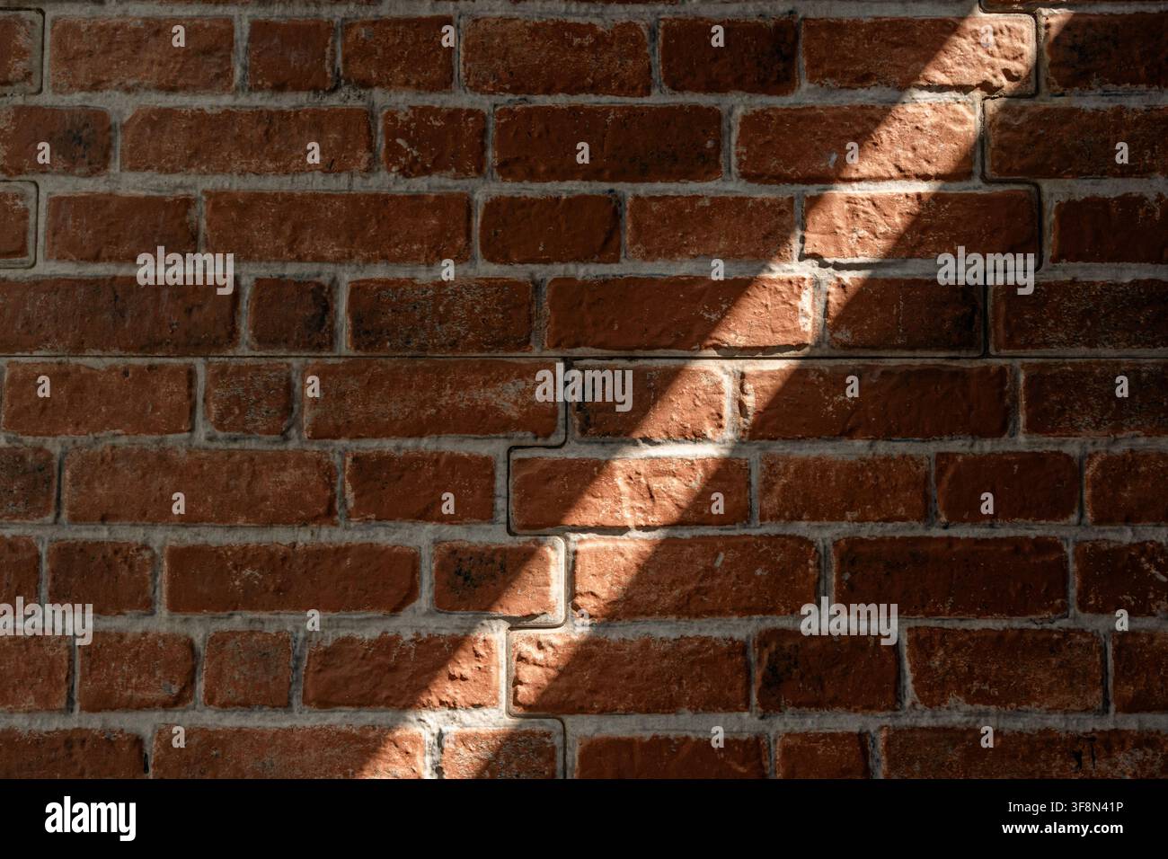 Red brick wall texture with a distinct diagonal shadow cast across. Stock Photo