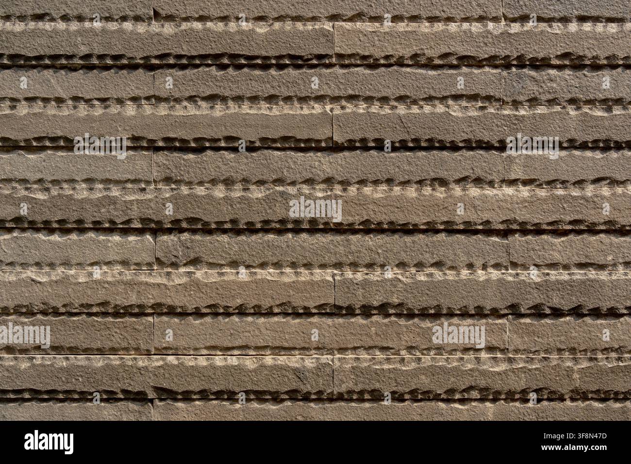 Textured brown stone wall cladding with horizontal chiseled ribbed pattern background. Stock Photo