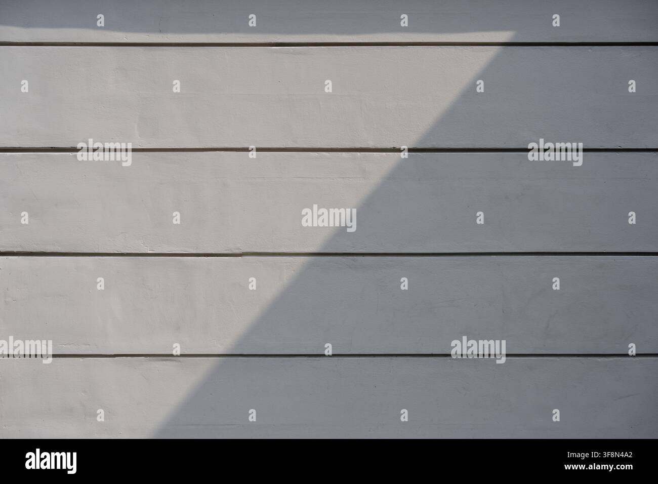 Light grey wall texture with horizontal grooves featuring a sharp diagonal shadow cast across the surface. Stock Photo